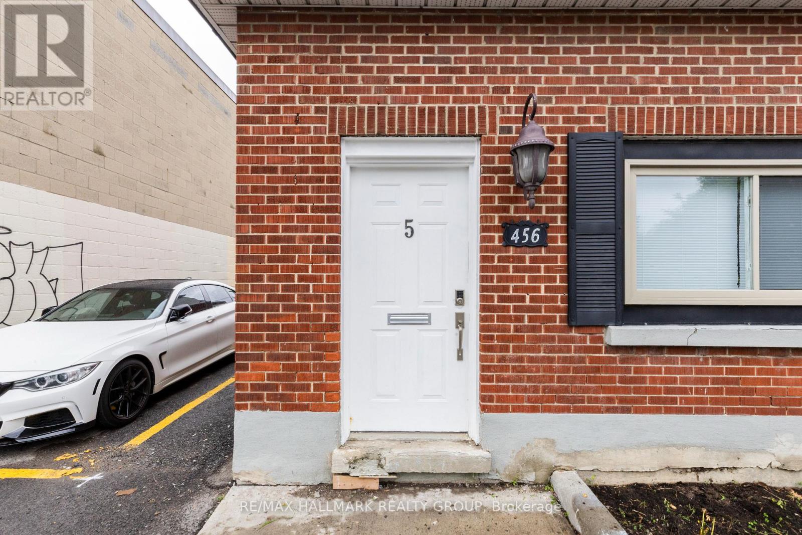 A white car is parked in front of a building with a sign that reads "RE/MAX Pallmark Realty Group Brokerage.".