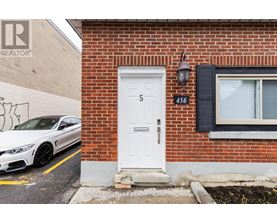 A white car is parked in front of a building with a sign that reads "RE/MAX Pallmark Realty Group Brokerage.".