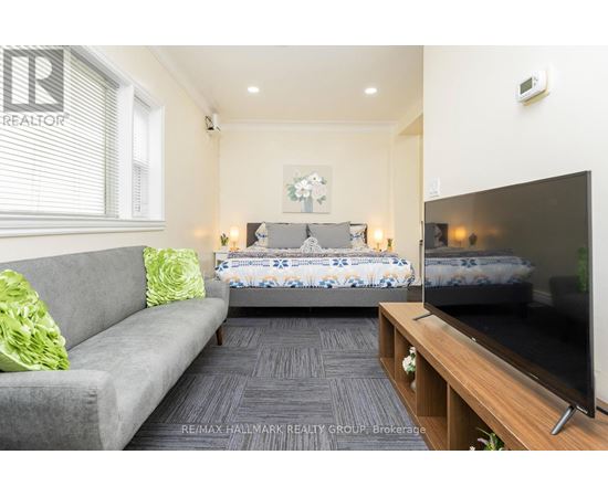 A living room with a grey couch, a bed with a blue and white comforter, and a television on a wooden stand.