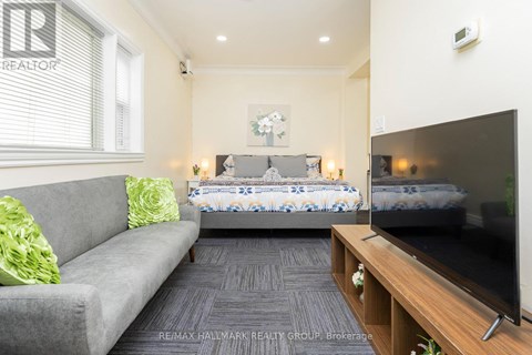 A living room with a grey couch, a bed with a blue and white comforter, and a television on a wooden stand.