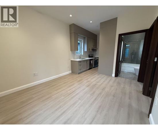 A spacious room with light wood flooring and a kitchen area in the background.