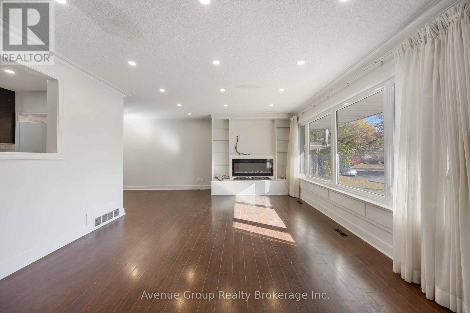 A spacious room with wooden floors and a large window with white curtains.
