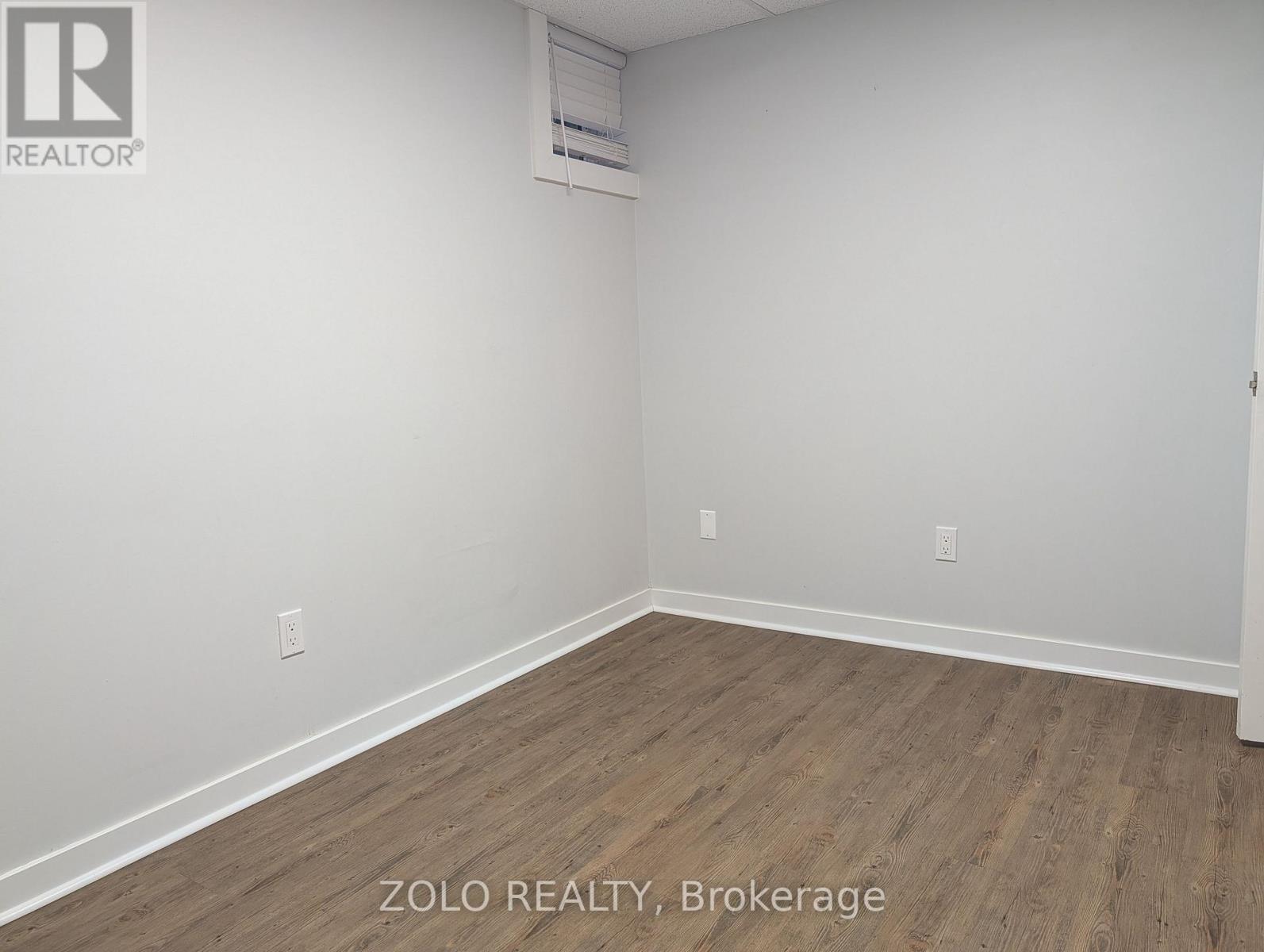 A room with wooden flooring and white walls, with a logo that reads "REALTOR" in the top left corner.