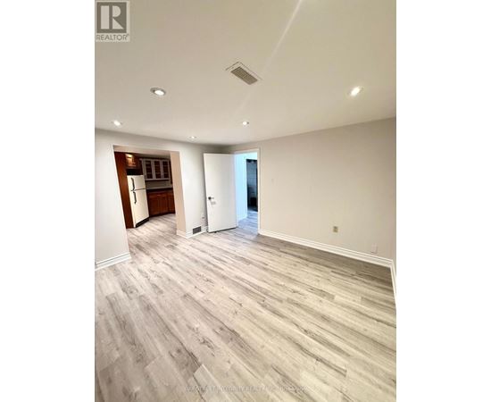 A spacious room with wood flooring and a kitchen area in the background.