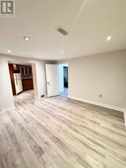 A spacious room with wood flooring and a kitchen area in the background.