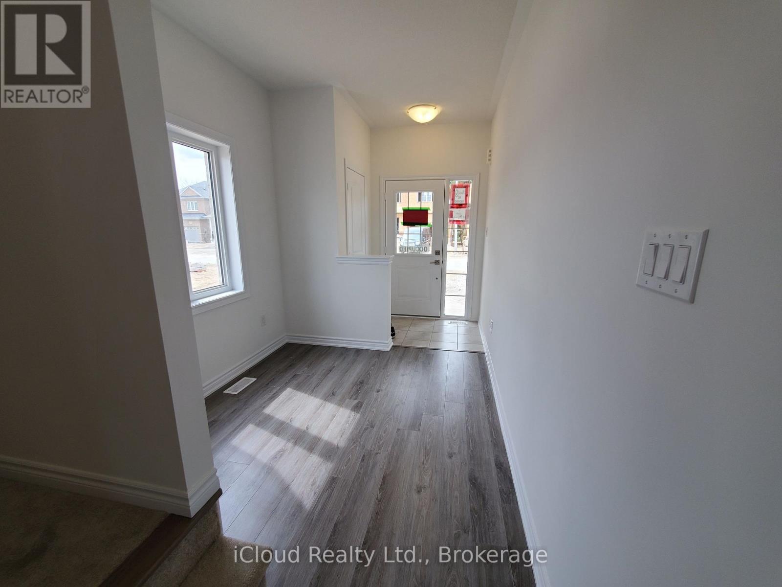 A room with wooden flooring and white walls, with a window on the left and a door on the right.