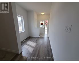 A room with wooden flooring and white walls, with a window on the left and a door on the right.