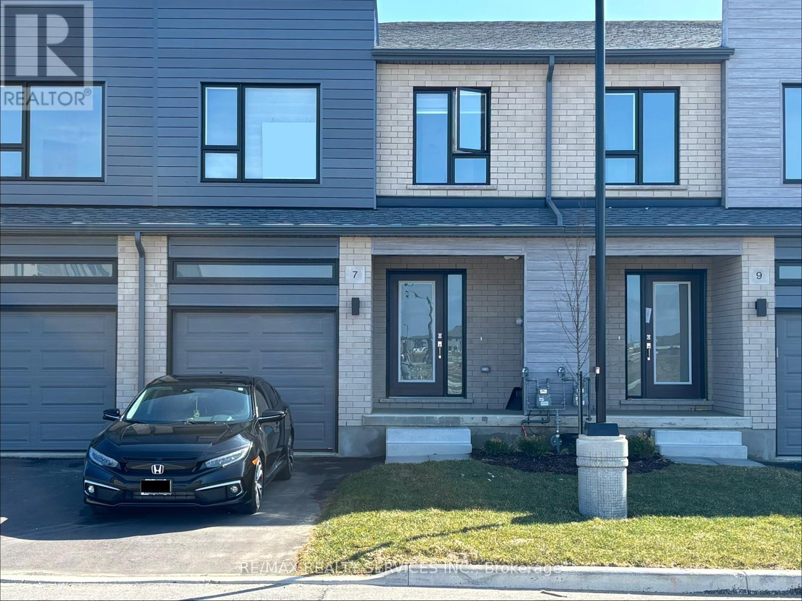 A black car is parked in front of a house with a REALTOR sign on the window.