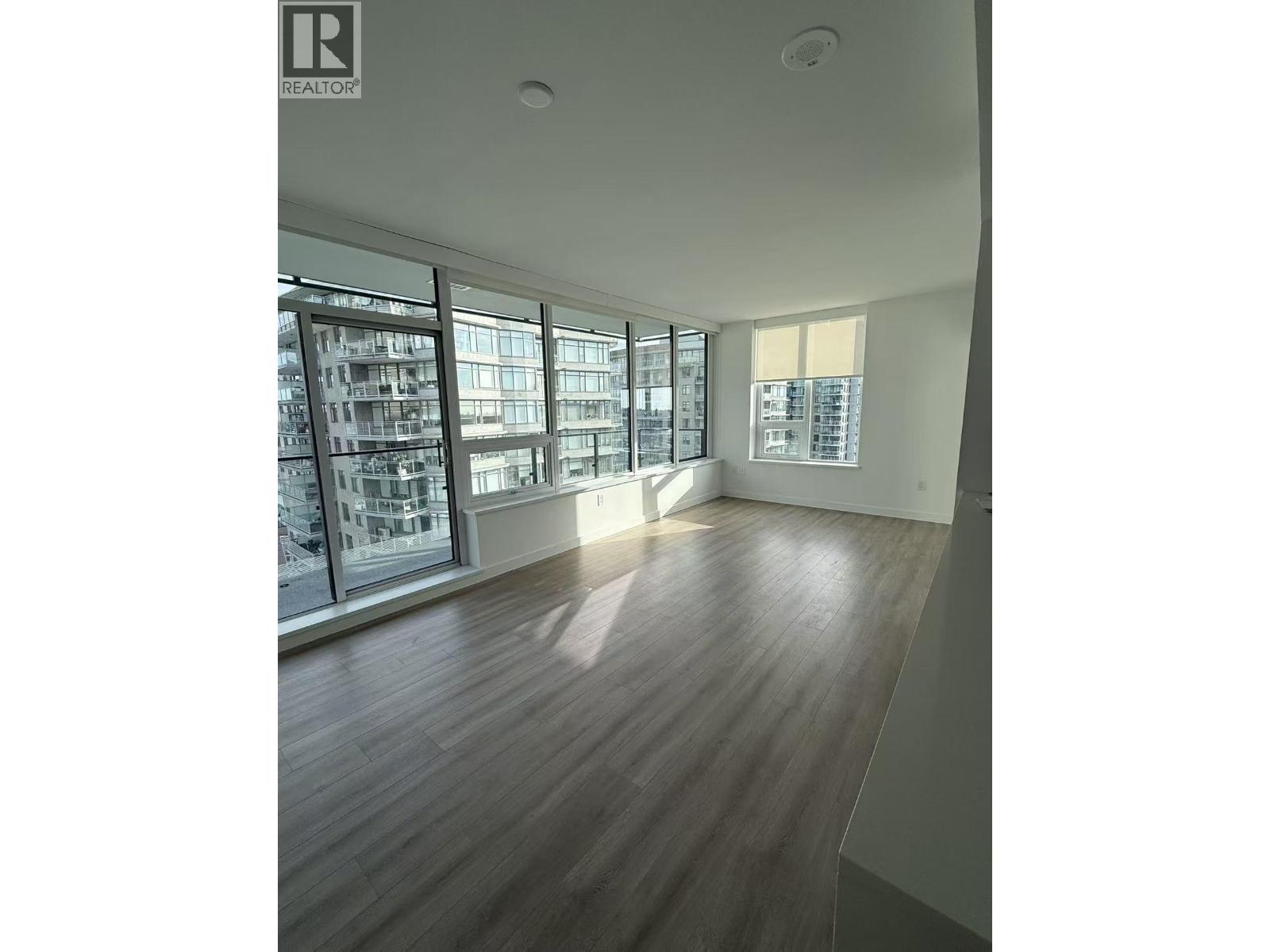 A spacious room with wooden flooring and large windows.