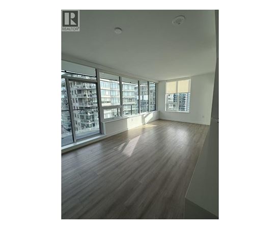 A spacious room with wooden flooring and large windows.