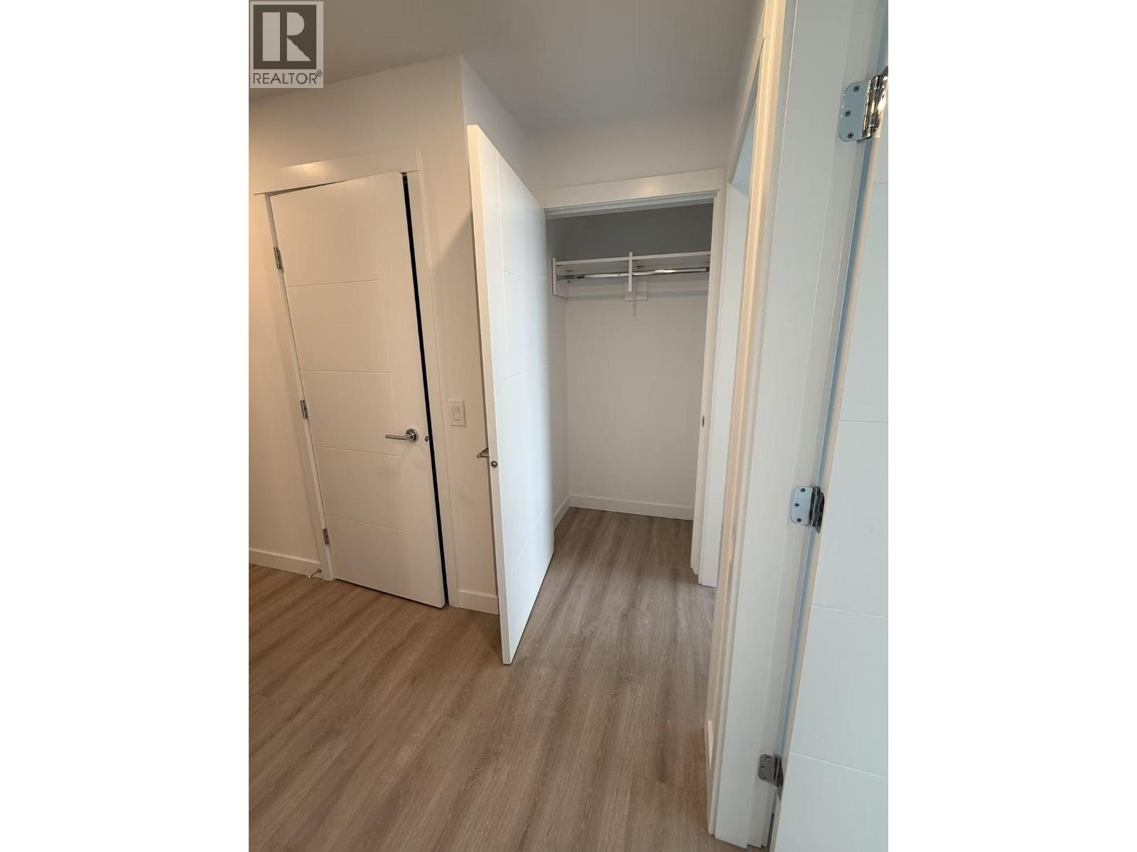A white door is open to a room with a white wall and a white closet with a coat rack.