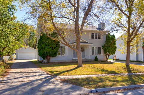 A house with a white garage door is surrounded by trees with yellow leaves.