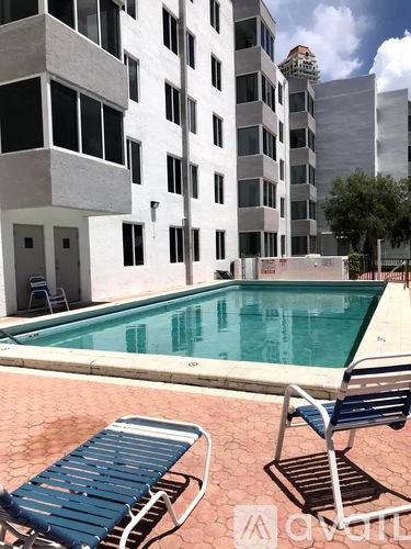 A pool in front of a white building with a blue chair in the foreground.