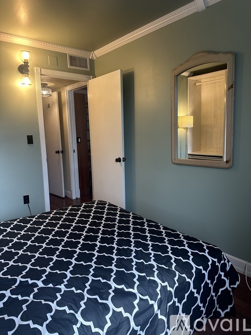 A bedroom with a patterned bedspread and a mirror above it.