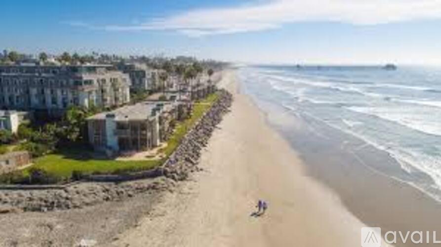 A beach with a row of buildings on the left and people walking on the beach.