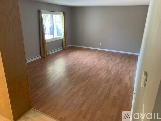A room with wooden flooring and a window with curtains.