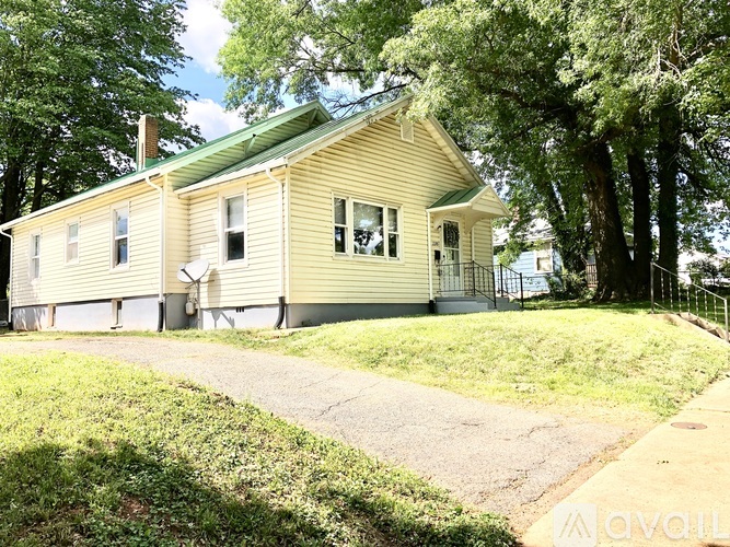 A small yellow house with a green roof is surrounded by trees.