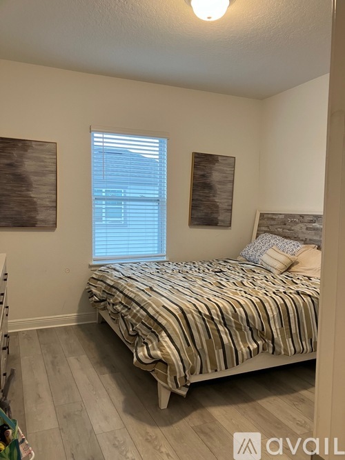 A bedroom with a bed, a window with blinds, and two pictures on the wall.