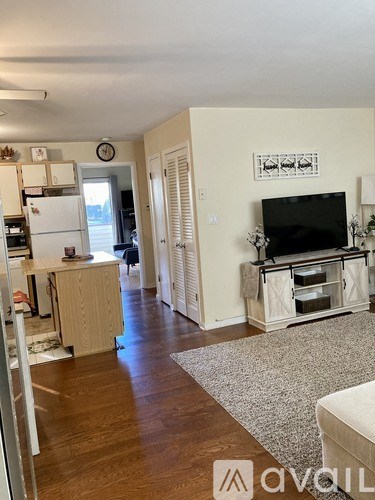 A living room with a television and a refrigerator in the kitchen.