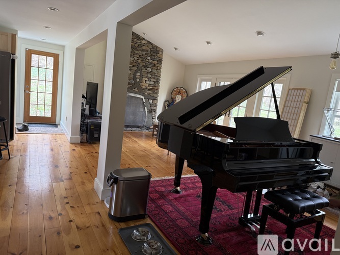 A grand piano sits in a spacious room with wooden floors and a stone wall.