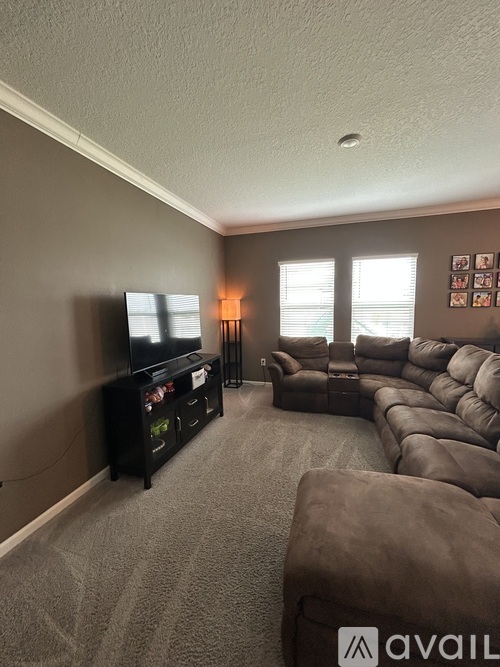 A living room with a grey carpet and brown furniture.