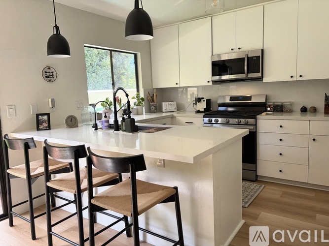 A kitchen with white cabinets and a white island with two chairs.