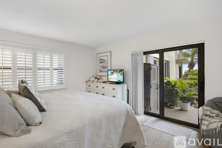 A bedroom with a large bed, a dresser with a mirror, and a sliding glass door leading to a balcony.