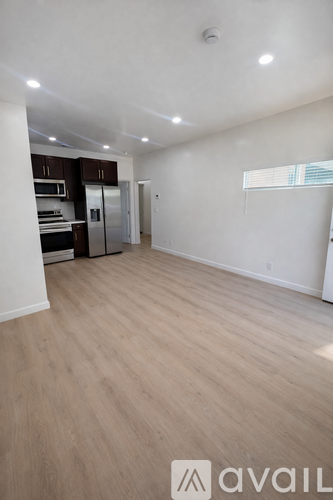 A spacious room with wooden flooring and a kitchen area with a refrigerator, sink, and cabinets.