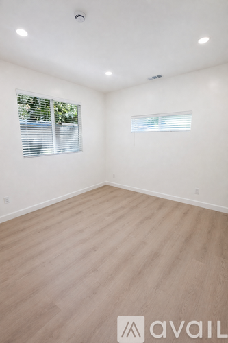 A room with wooden flooring and two windows with blinds.