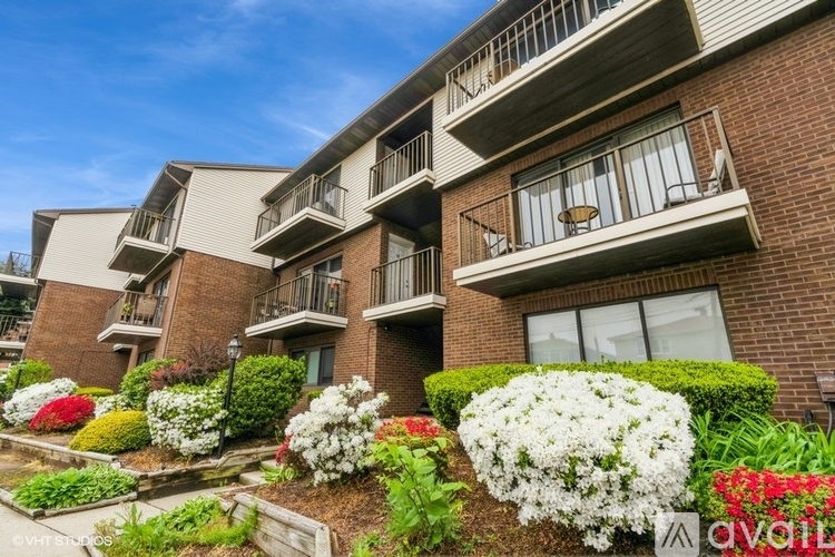 A row of apartment buildings with balconies and flower beds in front.