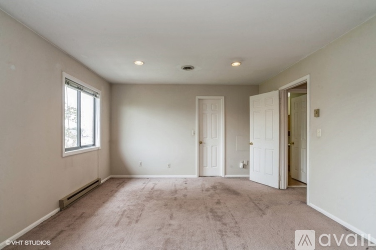 A spacious room with carpeted floor, two doors, and a window.