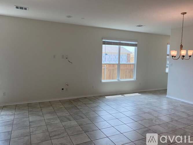 A spacious room with tiled flooring and a window overlooking a wooden fence.