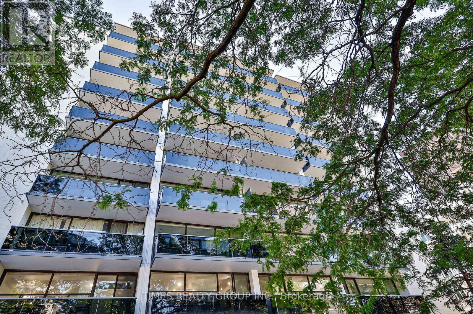 A tall building with balconies and trees in the foreground.