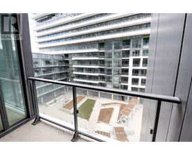 A balcony with a glass door and a metal railing overlooks a courtyard with a grassy area and several benches.