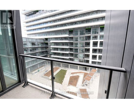 A balcony with a glass door and a metal railing overlooks a courtyard with a grassy area and several benches.