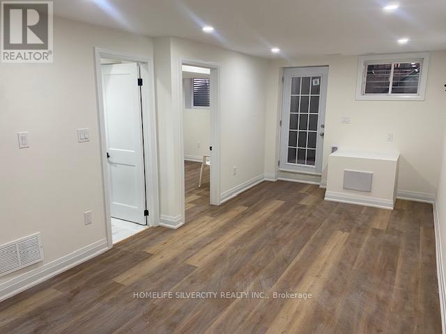A room with wooden flooring and white walls, with a door on the left and a window on the right.