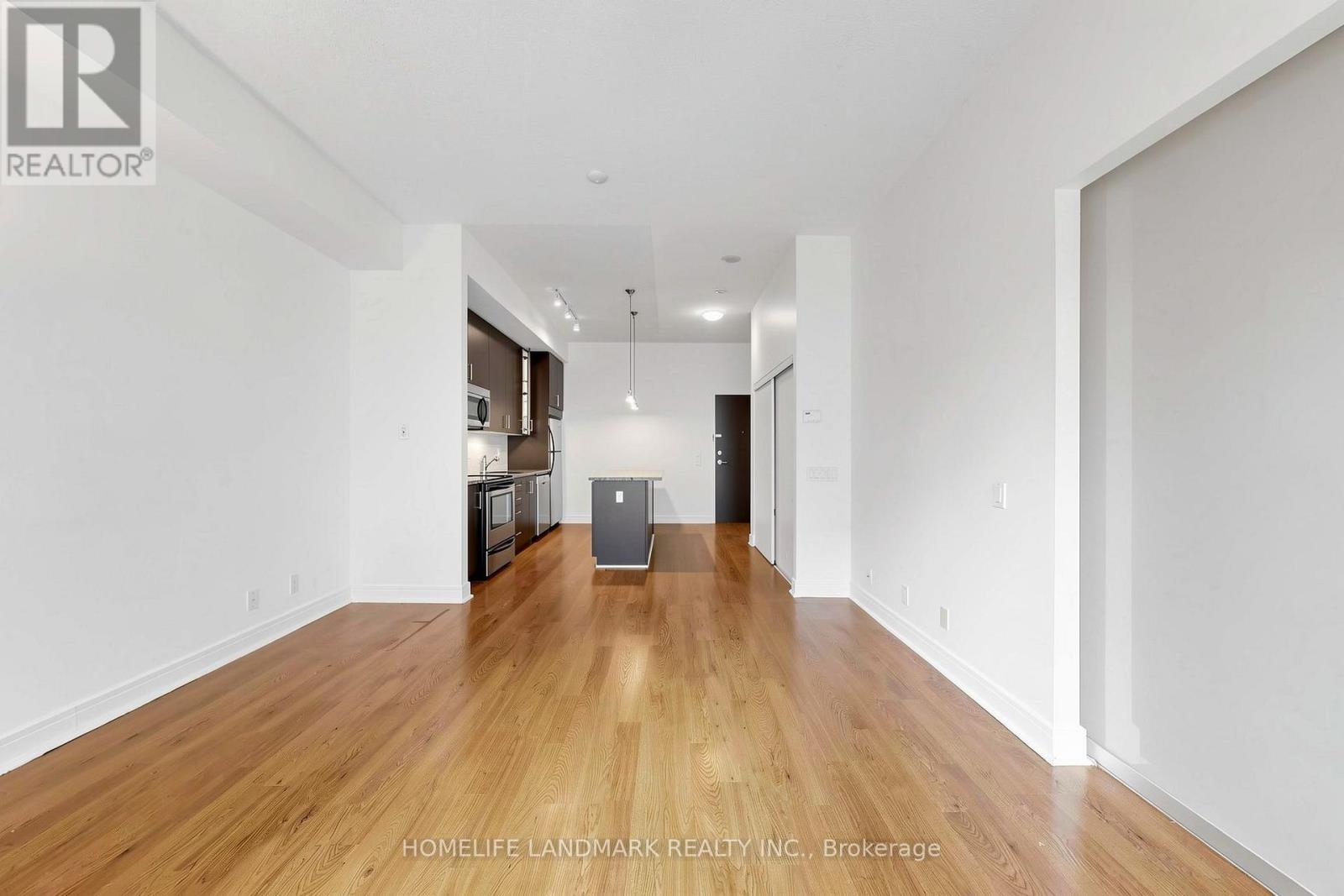 A spacious room with wooden floors and white walls, furnished with a kitchenette.