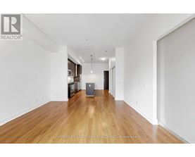 A spacious room with wooden floors and white walls, furnished with a kitchenette.