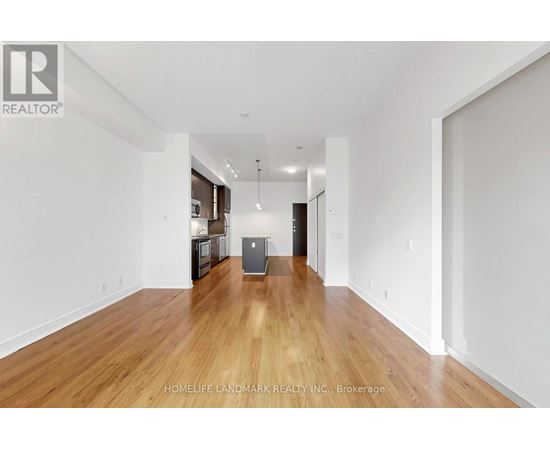A spacious room with wooden floors and white walls, furnished with a kitchenette.