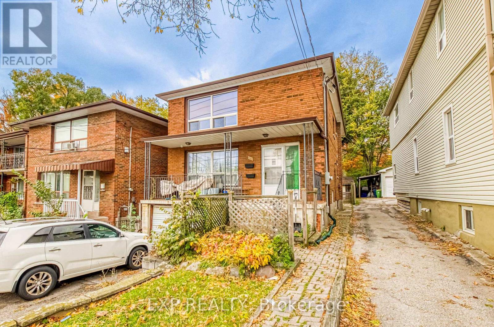 A white car is parked in front of a brick house.