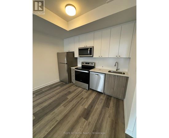 A kitchen with a refrigerator, microwave, oven, and sink.