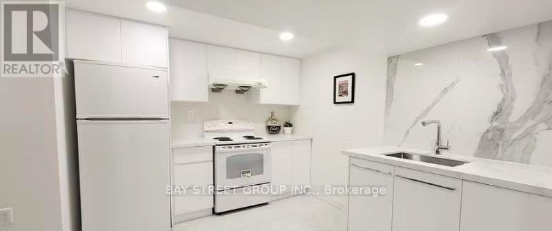 A white kitchen with a refrigerator, sink, and cabinets.