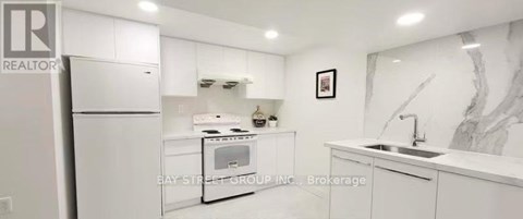 A white kitchen with a refrigerator, sink, and cabinets.