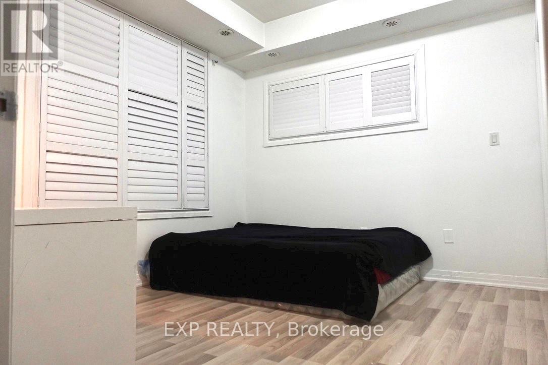 A bedroom with a bed, wooden flooring, and white shutters.