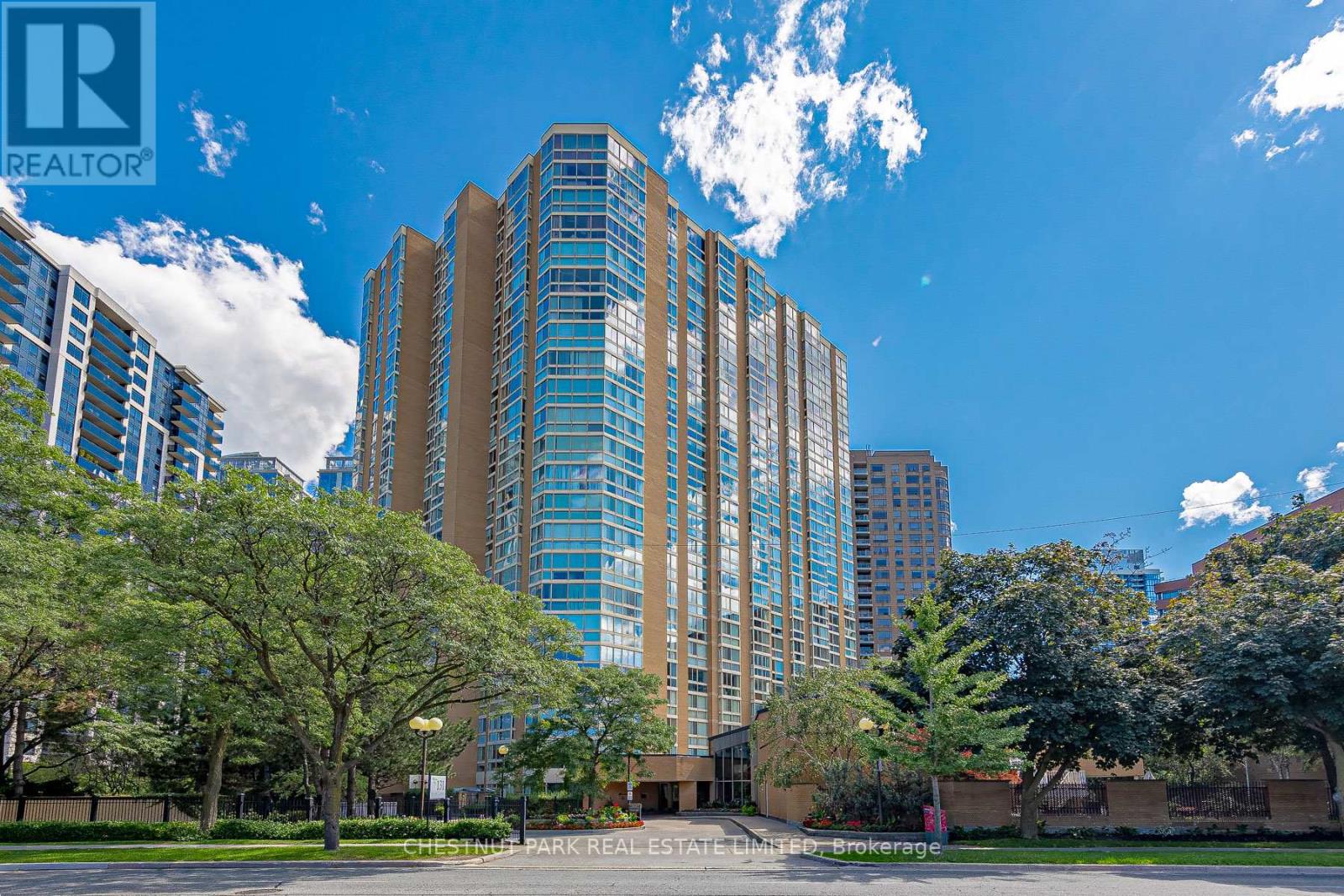 A tall building with a glass facade is surrounded by trees and other buildings.