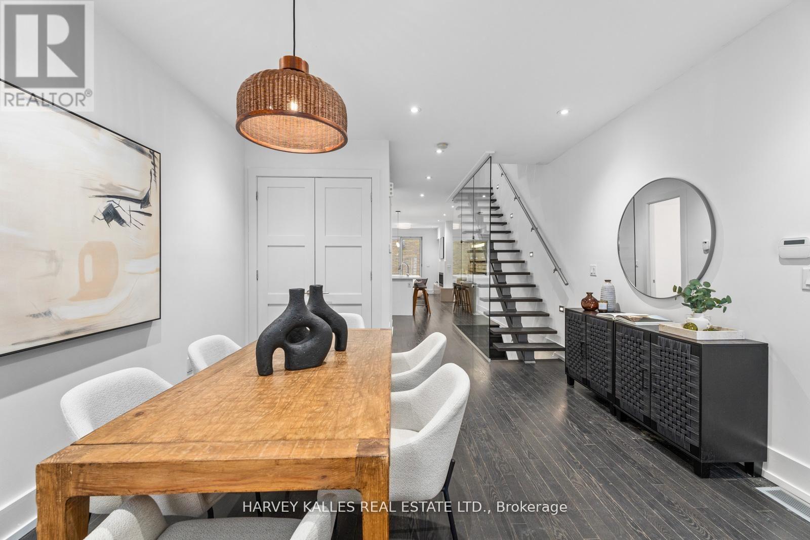 A dining room with a wooden table and chairs, a staircase, and a round mirror on the wall.