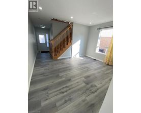 A spacious room with a wooden staircase and grey flooring.