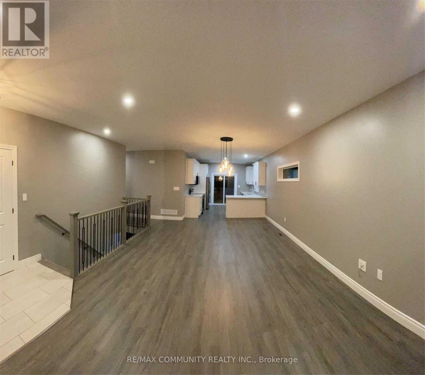 A spacious room with wooden flooring and a staircase on the left side.