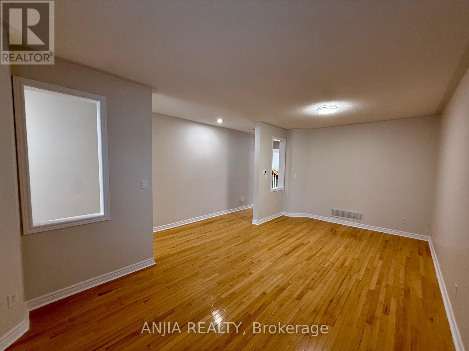 A room with wooden flooring and white walls, with a window on the left wall.