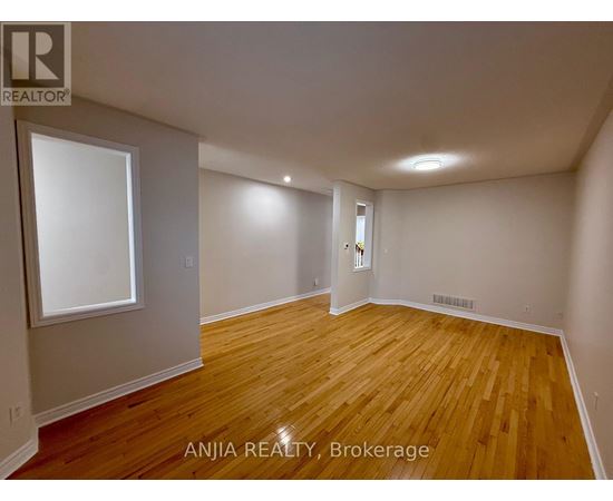 A room with wooden flooring and white walls, with a window on the left wall.